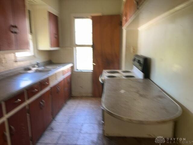 kitchen with white electric stove, light countertops, a sink, and brown cabinets