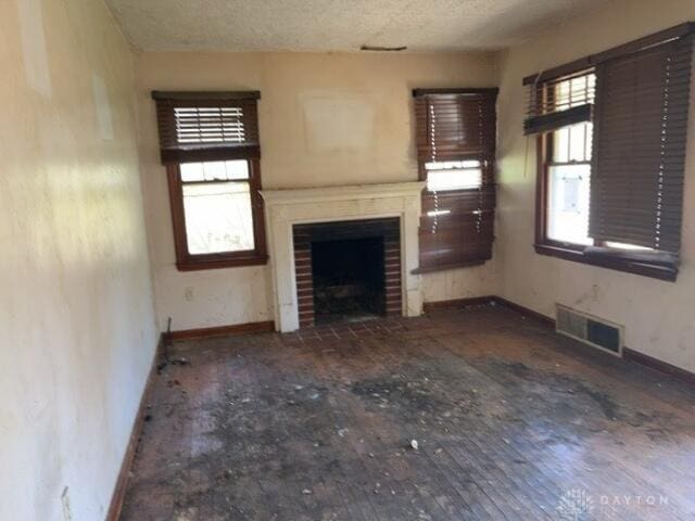 unfurnished living room featuring a fireplace with flush hearth, a textured ceiling, visible vents, and baseboards