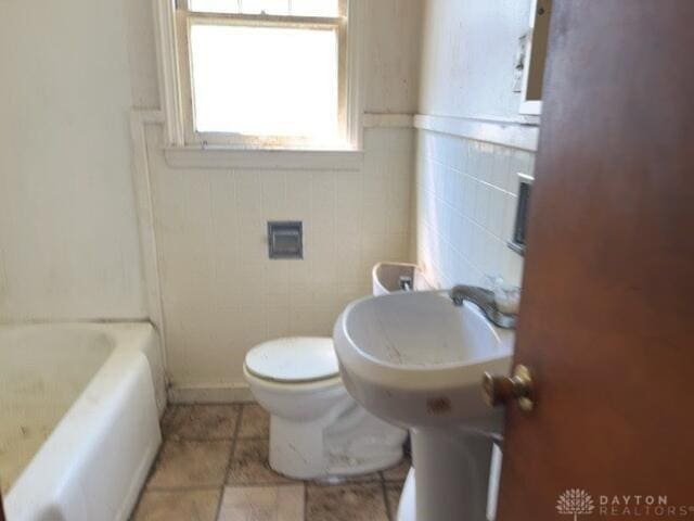 bathroom with a tub to relax in, tile patterned flooring, and toilet