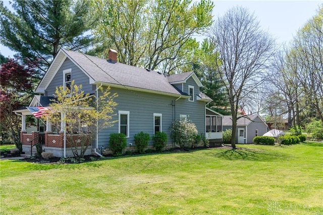 view of side of property featuring a chimney, a sunroom, a yard, and roof with shingles