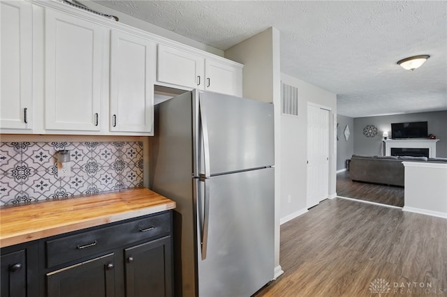kitchen featuring white cabinets, wood finished floors, visible vents, freestanding refrigerator, and decorative backsplash