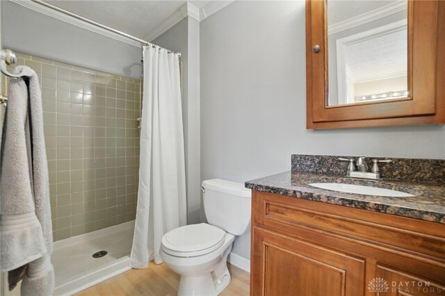 bathroom featuring a stall shower, toilet, wood finished floors, crown molding, and vanity