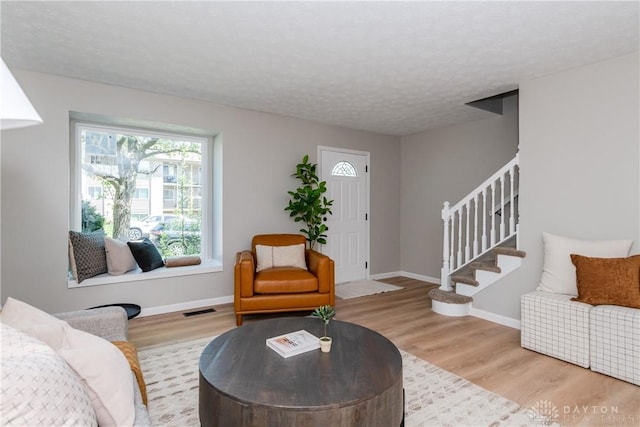 living area with baseboards, wood finished floors, visible vents, and stairs