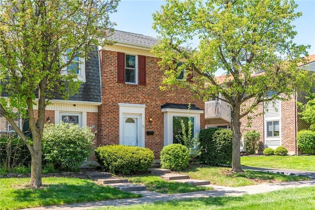 view of front facade featuring brick siding, roof with shingles, and a front yard