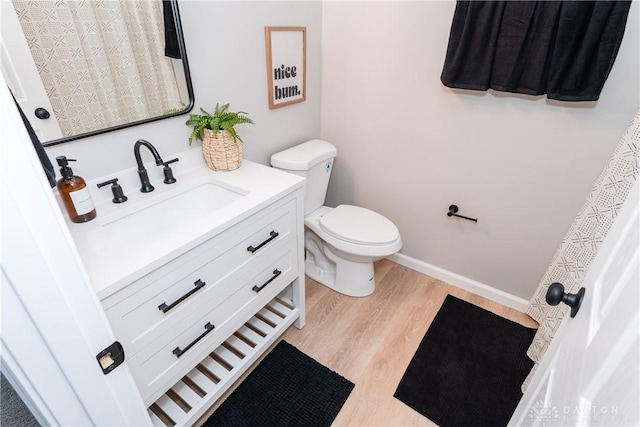 bathroom with baseboards, wood finished floors, toilet, and vanity