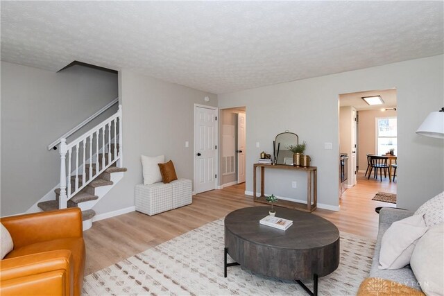 living room featuring stairway, baseboards, wood finished floors, and a textured ceiling