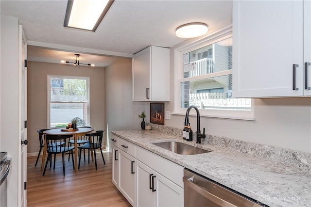 kitchen with a sink, light wood-type flooring, stainless steel appliances, white cabinetry, and light stone countertops