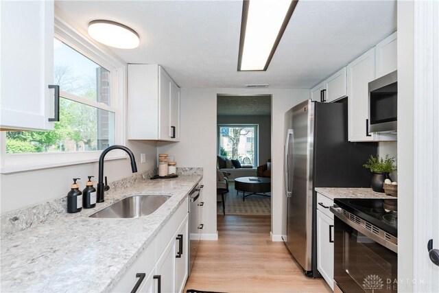 kitchen featuring white cabinets, a sink, light wood-style floors, light stone counters, and appliances with stainless steel finishes