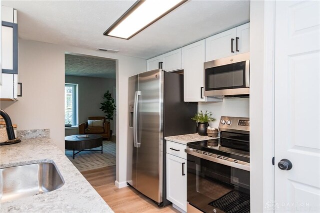 kitchen featuring white cabinets, visible vents, a sink, light wood-style floors, and appliances with stainless steel finishes