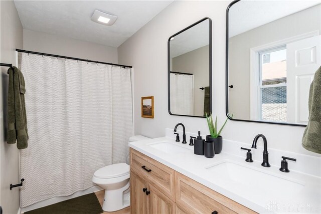 bathroom featuring a shower with shower curtain, double vanity, toilet, and a sink