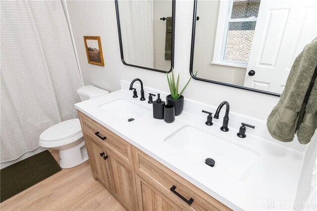 full bath featuring double vanity, wood finished floors, toilet, and a sink