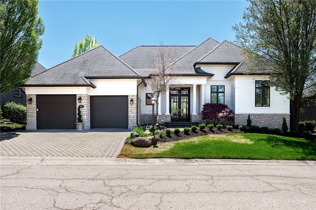 view of front of property with an attached garage, driveway, french doors, stone siding, and a front yard