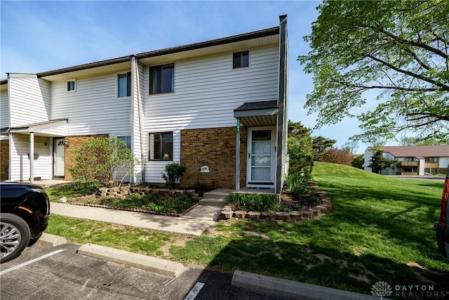 townhome / multi-family property featuring a front yard, uncovered parking, and brick siding
