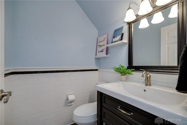 half bathroom with lofted ceiling, vanity, toilet, and wainscoting