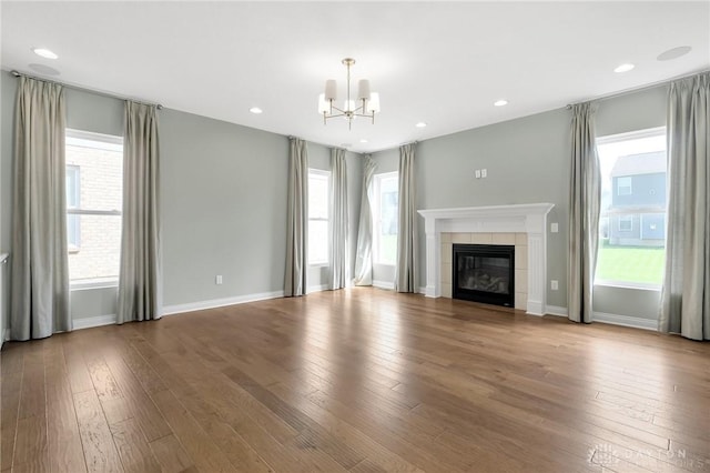 unfurnished living room featuring a tiled fireplace, a wealth of natural light, hardwood / wood-style floors, and a chandelier