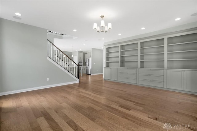 unfurnished living room featuring a notable chandelier, recessed lighting, baseboards, wood finished floors, and stairway