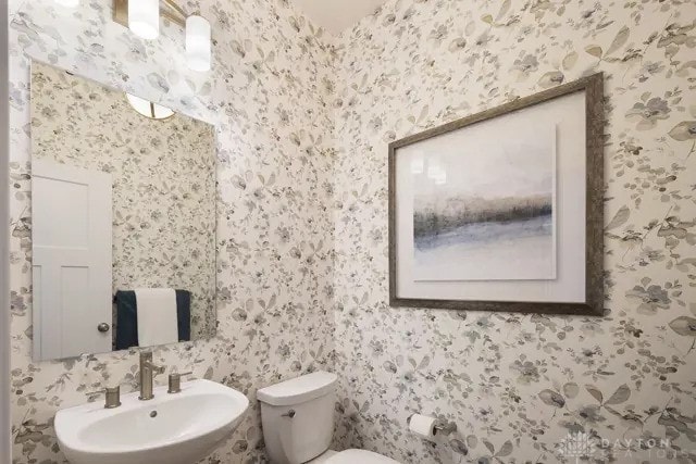 bathroom featuring a sink, toilet, and wallpapered walls