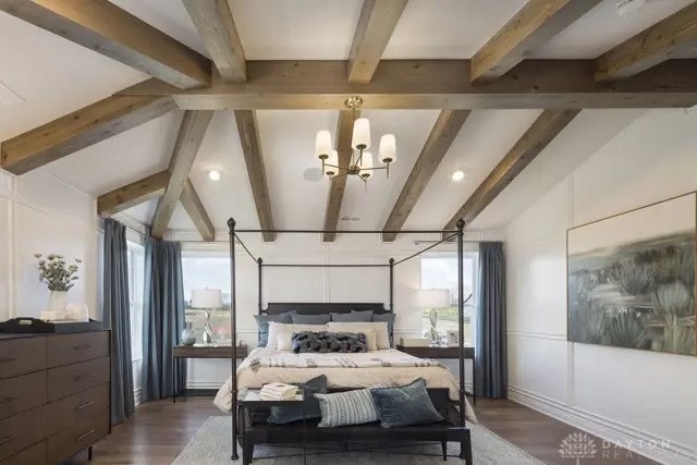 bedroom featuring lofted ceiling with beams, wood finished floors, and a notable chandelier