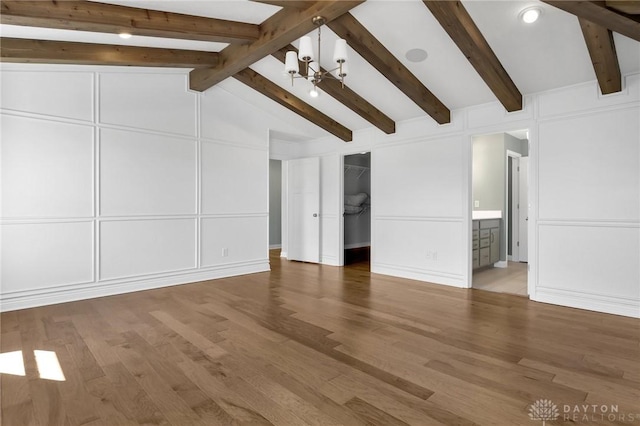 unfurnished living room featuring vaulted ceiling with beams, wood finished floors, a decorative wall, and an inviting chandelier