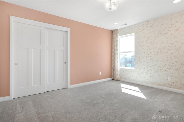 unfurnished bedroom featuring visible vents, baseboards, a closet, carpet flooring, and wallpapered walls