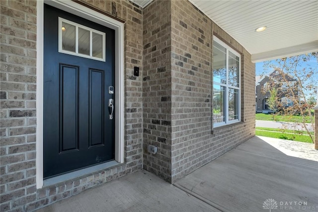 doorway to property featuring a porch and brick siding