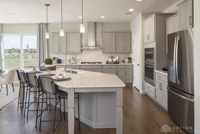 kitchen with a breakfast bar area, light countertops, wall chimney exhaust hood, a sink, and appliances with stainless steel finishes