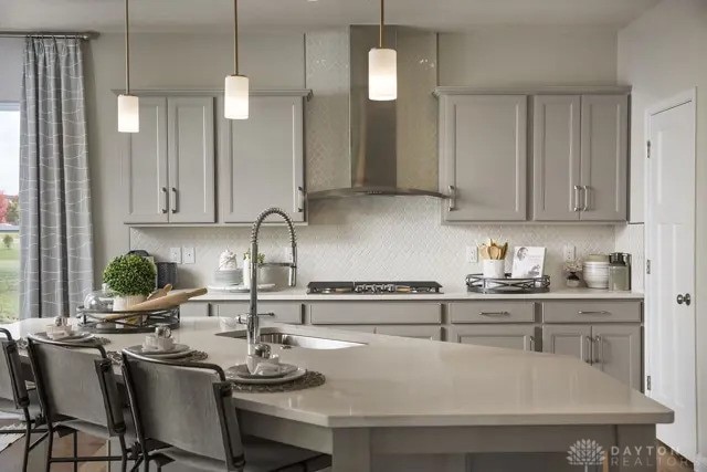 kitchen with gas cooktop, decorative backsplash, a sink, gray cabinetry, and wall chimney exhaust hood
