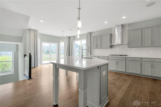 kitchen featuring wall chimney range hood, light countertops, a sink, cooktop, and gray cabinetry