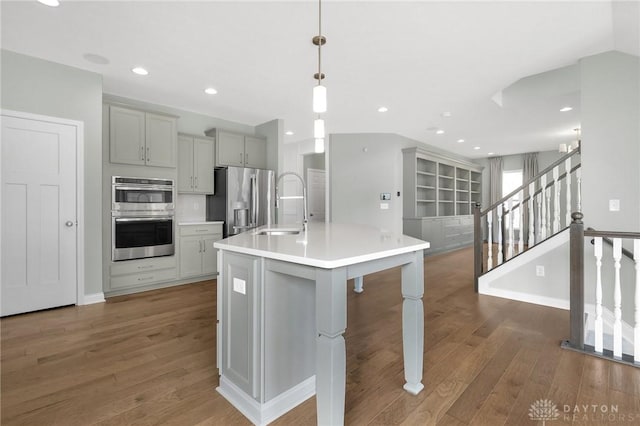 kitchen with stainless steel appliances, gray cabinets, a sink, and wood finished floors