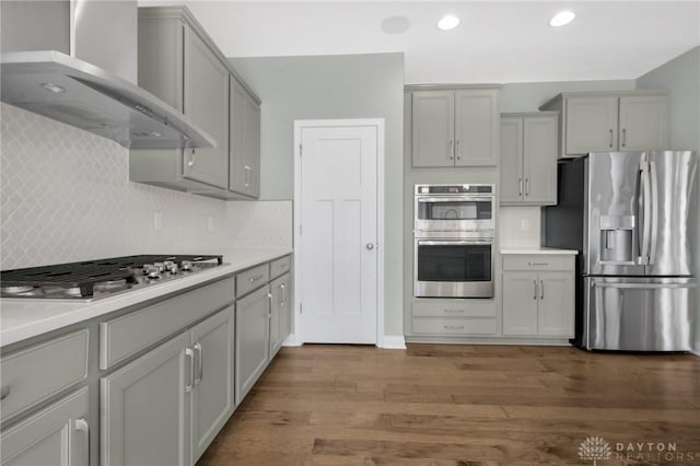 kitchen with wall chimney range hood, appliances with stainless steel finishes, gray cabinets, and wood finished floors