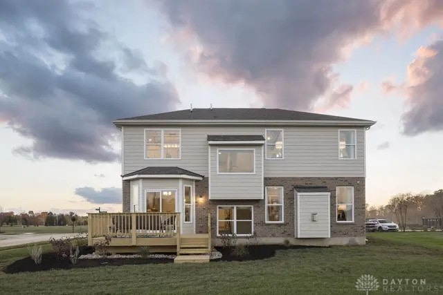 back of property at dusk with a wooden deck, a yard, and brick siding