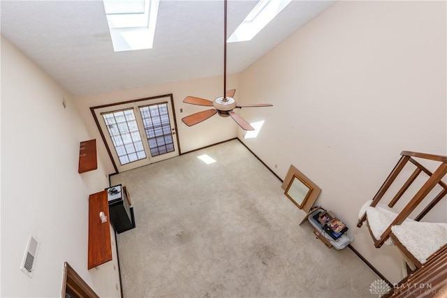 unfurnished living room featuring lofted ceiling with skylight, carpet floors, a ceiling fan, and visible vents