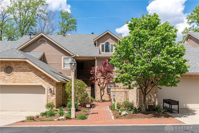 view of front of house featuring roof with shingles, concrete driveway, brick siding, an attached garage, and a balcony