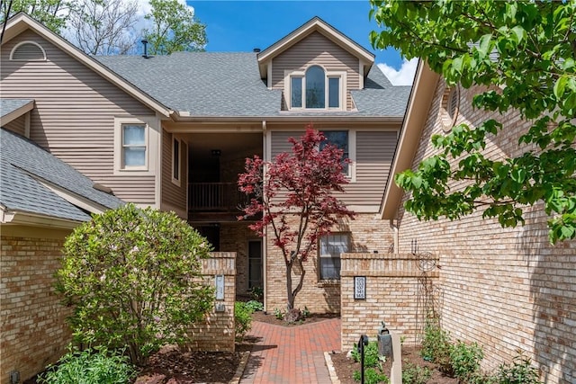 view of front facade featuring brick siding, a balcony, and a shingled roof