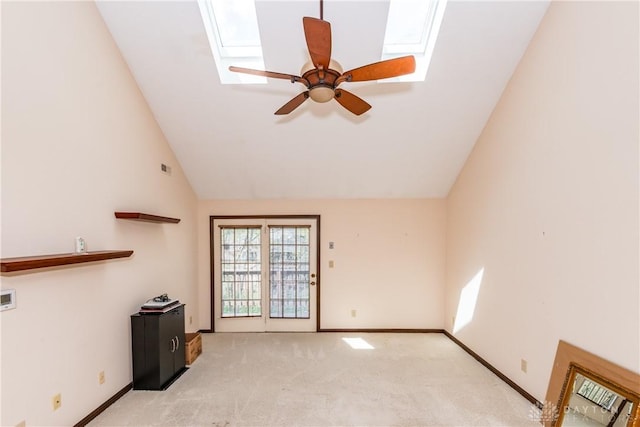 unfurnished living room with light carpet, a ceiling fan, vaulted ceiling with skylight, and baseboards