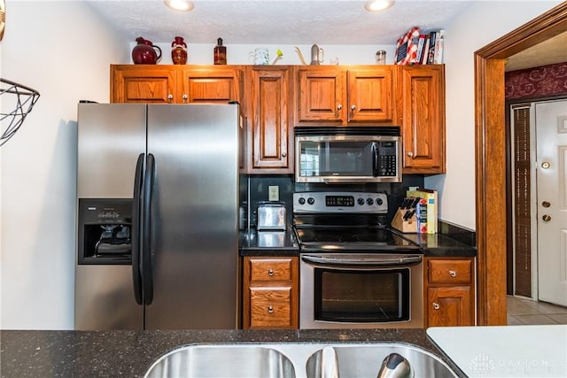 kitchen with dark stone counters, brown cabinets, appliances with stainless steel finishes, and tile patterned flooring