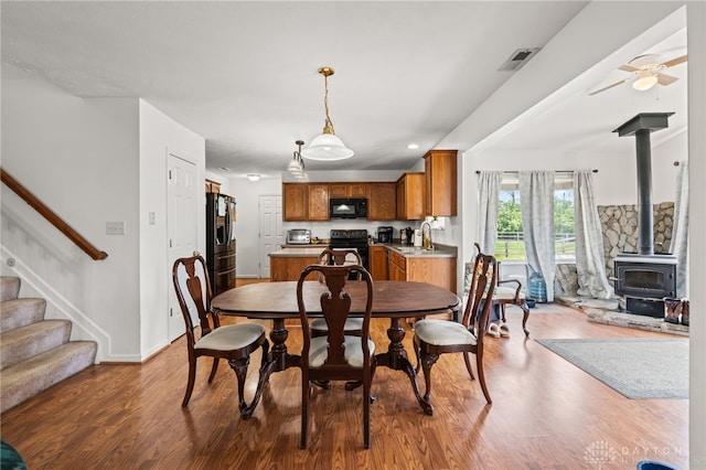 dining room featuring stairs, a wood stove, wood finished floors, and visible vents