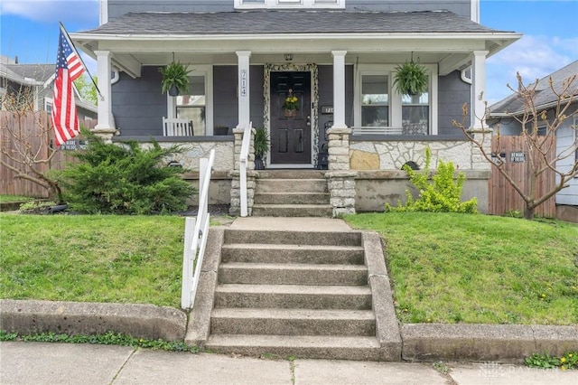 view of front of property with a front yard, roof with shingles, and a porch