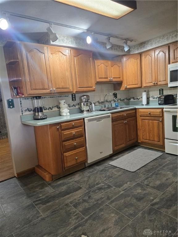 kitchen with a sink, brown cabinets, rail lighting, white appliances, and light countertops
