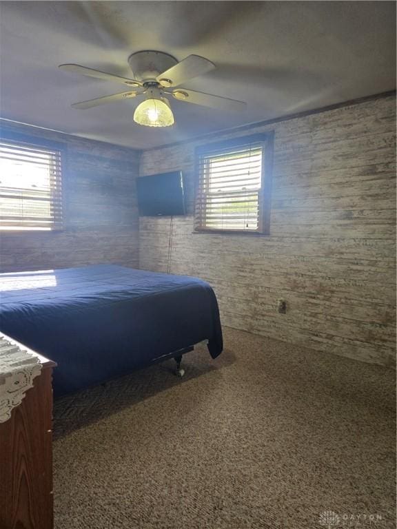 bedroom with wooden walls, a ceiling fan, and carpet floors