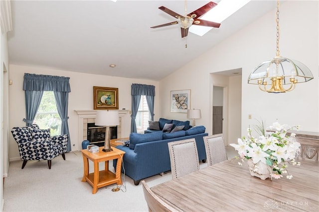 living room featuring ceiling fan with notable chandelier, a skylight, a tiled fireplace, and plenty of natural light