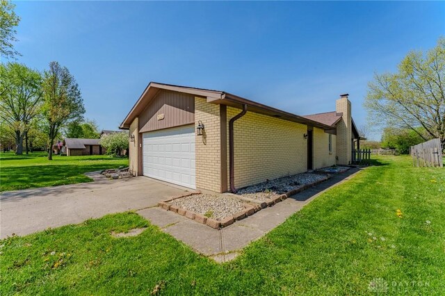 view of side of home featuring a chimney, brick siding, fence, a garage, and a lawn