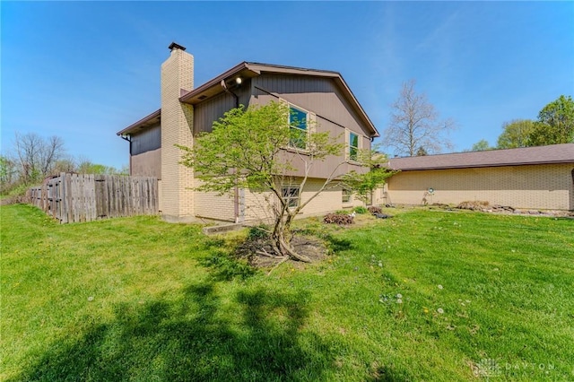 view of property exterior featuring a chimney, brick siding, fence, and a lawn