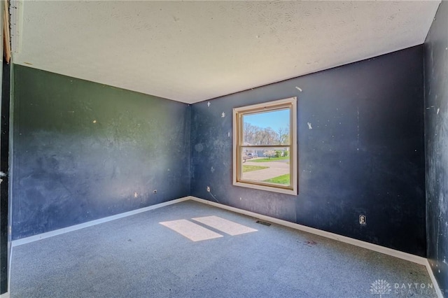 carpeted spare room featuring a textured ceiling, visible vents, and baseboards