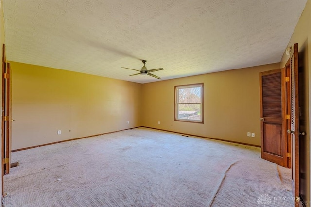 carpeted spare room featuring a textured ceiling, ceiling fan, and baseboards