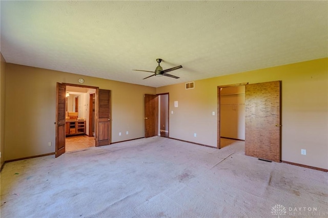unfurnished bedroom featuring baseboards, ensuite bathroom, a walk in closet, and light colored carpet