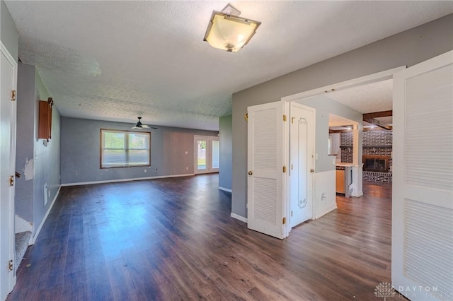 empty room with dark wood-style flooring, a fireplace, ceiling fan, baseboards, and a textured ceiling