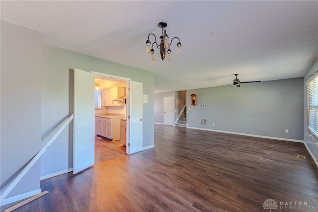 unfurnished living room with stairs, visible vents, baseboards, wood finished floors, and ceiling fan with notable chandelier