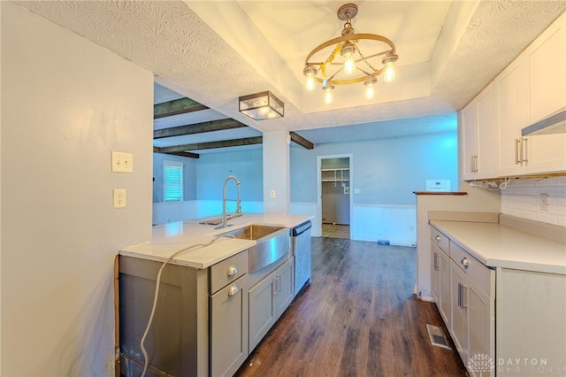 kitchen featuring a sink, a raised ceiling, light countertops, dishwasher, and dark wood-type flooring
