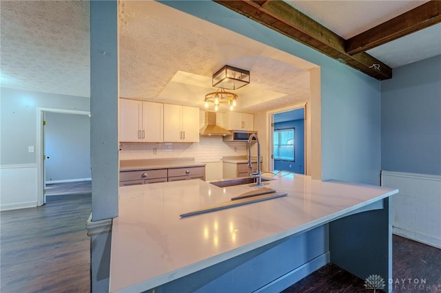 kitchen featuring stainless steel microwave, a sink, dark wood-style flooring, wall chimney exhaust hood, and white cabinetry